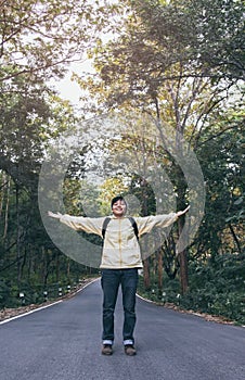 Asian young man in Yellow long shirt and grey hat hiking standing open arm happy at the road with tree mountain peak above Hiker