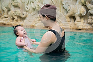 Asian young mother and adorable curly little baby girl having fun in a swimming pool