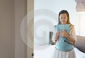 Asian young mother with her son in a baby carrier in bedroom,Feeling happy