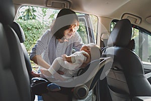 Asian young mother putting her baby son into car seat