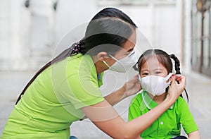 Asian young mother wearing protective mask for her daughter while outside to against PM 2.5 air pollution in Bangkok city.