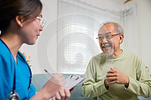 Asian young nurse writing prescription during home visit sick elder old man