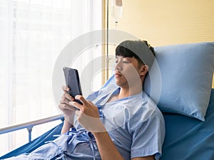 Asian young patient boy use smartphone for contact insurance and claim admit by himself in the bedroom at hospital