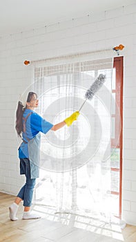 Asian young professional cleaning service woman worker working in the house. The girl cleans the curtain and window.