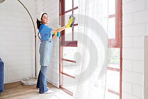 Asian young professional cleaning service woman worker working in the house. The girl cleans glass window by wiping it with rag