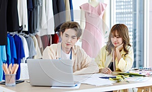 Asian young professional talent male female dressmaker designer seamstress colleague with measuring tape sitting at working table