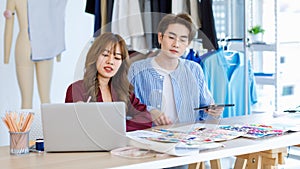 Asian young professional talent male female dressmaker designer seamstress colleague with measuring tape sitting at working table