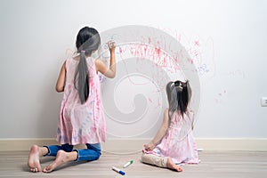 Asian young sibling kid girl enjoy paint on white wall in living room. Little adorable children having fun drawing and coloring