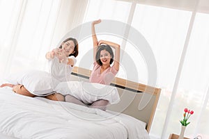 Asian young sisters lovely couple sitting on white bed and holding hands together in bedroom