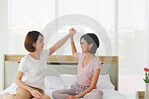 Asian young sisters lovely couple sitting on white bed and holding hands together in bedroom. Homosexual women or Lesbian in love