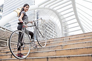 asian young sport woman in sportswear holding a bicycle up stairs in city