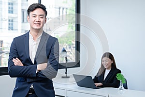 Asian young successful businessman wear formal suit smiling with confident and standing with crossed arm at office