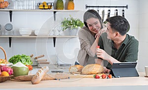 Asian young sweet couple cooking breakfast together in home kitchen. Beautiful wife smiling embracing her husband from back while