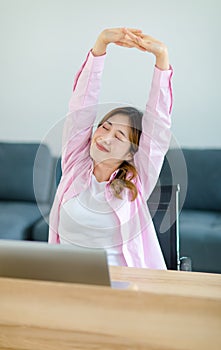 Asian young teenage female freelancer worker sitting smiling while working with laptop notebook computer at workstation