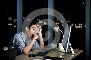 Asian young tired staff officer yawning during using desktop computer, feeling sleepy after having overwork project overnight,