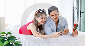 Asian young traveler lover couple in casual outfit with sunglasses and hat laying down smiling together on bed holding passport