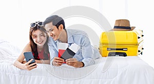 Asian young traveler lover couple in casual outfit with sunglasses and hat laying down smiling together on bed holding passport