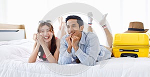 Asian young traveler lover couple in casual outfit with sunglasses and hat laying down smiling together on bed holding passport