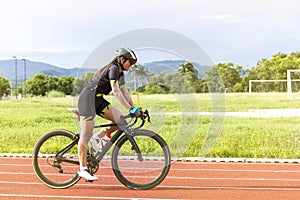 Asian young woman athletes cycling on a race track intently and happily at outdoor sports field in bright day
