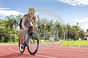 Asian young woman athletes cycling on a race track intently at outdoor sports field on bright day