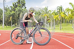 Asian young woman athletes rest stand and handle the bicycle on race track at outdoor sports field on bright day