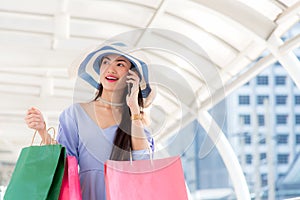 Asian young woman at the city with shopping bags talking on mobile phone.