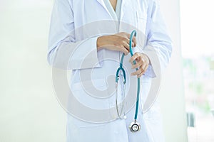 Asian Young   woman  doctor or nurse in white uniform scrubs holding Stethoscope standing in front of a white wall in the hospital