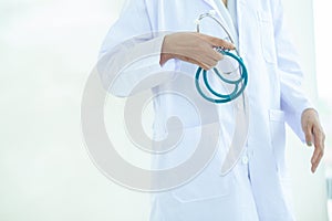 Asian Young   woman  doctor or nurse in white uniform scrubs holding Stethoscope standing in front of a white wall in the hospital