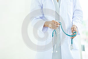 Asian Young   woman  doctor or nurse in white uniform scrubs holding Stethoscope standing in front of a white wall in the hospital
