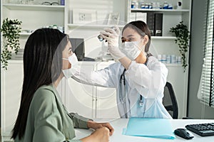 Asian young woman doctor using flashlight on patient`s eye in hospital. Attractive specialist physician wear mask, examining and