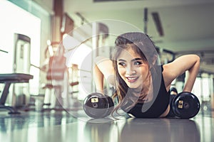 Asian young woman doing push ups with dumbbell on floor in fitness gym and equipment background. Workout and Sport Exercise