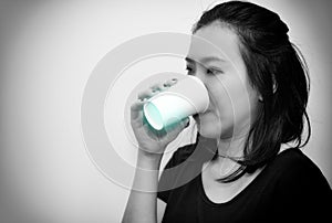 Asian young woman drinking a fresh white paper cup of water or other beverage. black and white tone