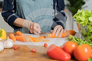 Asian young woman, girl or housewife using knife, cutting carrots on board, on wooden table in kitchen home, preparing ingredient