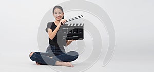 Asian young woman holding black clapper board or movie slate or clapboard and sit on thefloor .it use in video production ,film,