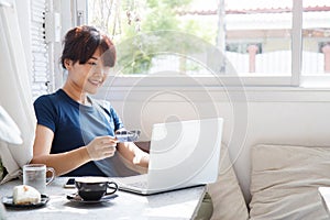Asian young woman holding credit card and using laptop computer.