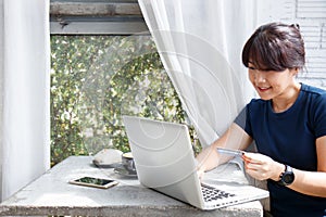 Asian young woman holding credit card and using laptop computer while sitting in cafe. Online shopping concept. Copy space.