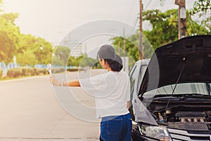 Asian young woman holding a wrench and hitch-hiking for help while the car broken down