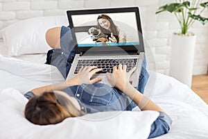 Asian young woman lying on bed and using computer laptop VDO Call Conference to meeting friend