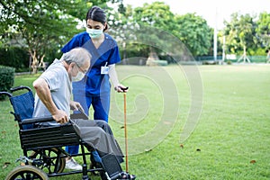 Asian young woman nurse at nursing home take care and support disabled senior elderly man on walker or cane at backyard. Caregiver