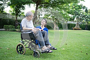 Asian young woman nurse at nursing home take care and support disabled senior elderly man on wheelchair at backyard. Beautiful