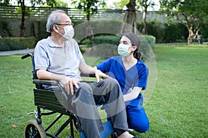 Asian young woman nurse at nursing home take care and support disabled senior elderly man on wheelchair at backyard. Caregiver