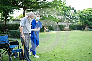 Asian young woman nurse taking care and support disabled senior elderly man on wheelchair at backyard. Caregiver doctor and older