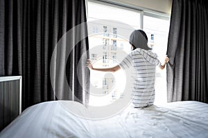 Asian young woman opening curtain and window for hygienic,sunlight to enter her bedroom and air circulate freely in room at home, photo