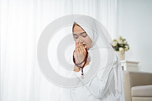 Asian young woman praying with Al-Qur`an and prayer beads