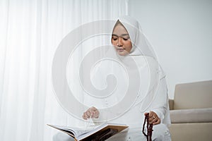 Asian young woman praying with Al-Qur`an and prayer beads