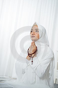 Asian young woman praying with Al-Qur`an and prayer beads