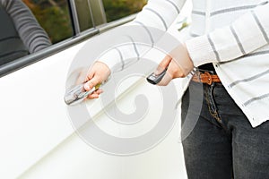 Asian young woman presses unlock button on remote control car key for opening car door.