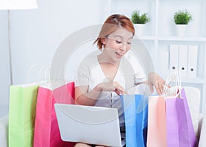 Asian young woman sitting on sofa with shopping bags using laptop computer to online shopping
