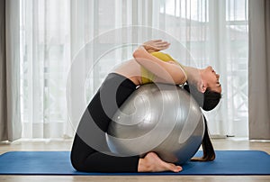 Asian young woman in sportswear doing abs exercises on a fitness ball for healthcare slim fit and body weight control at home