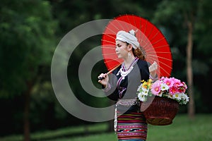 Asian young woman standing on green grass wearing traditional thai culture lanna dress style and basket of flowers and her red